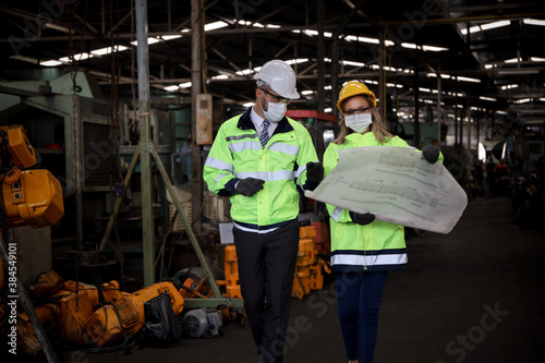 Manager or supervisor wear face mask talking or discussing with engineering team or worker about electrical drawing of machine control and operate in manufacturing factory, Covid or virus protection © torsakh