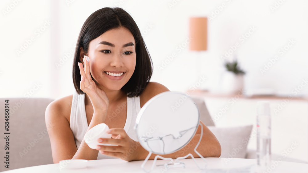 Young asian woman applying cream on her face Young asian woman applying cream on her face