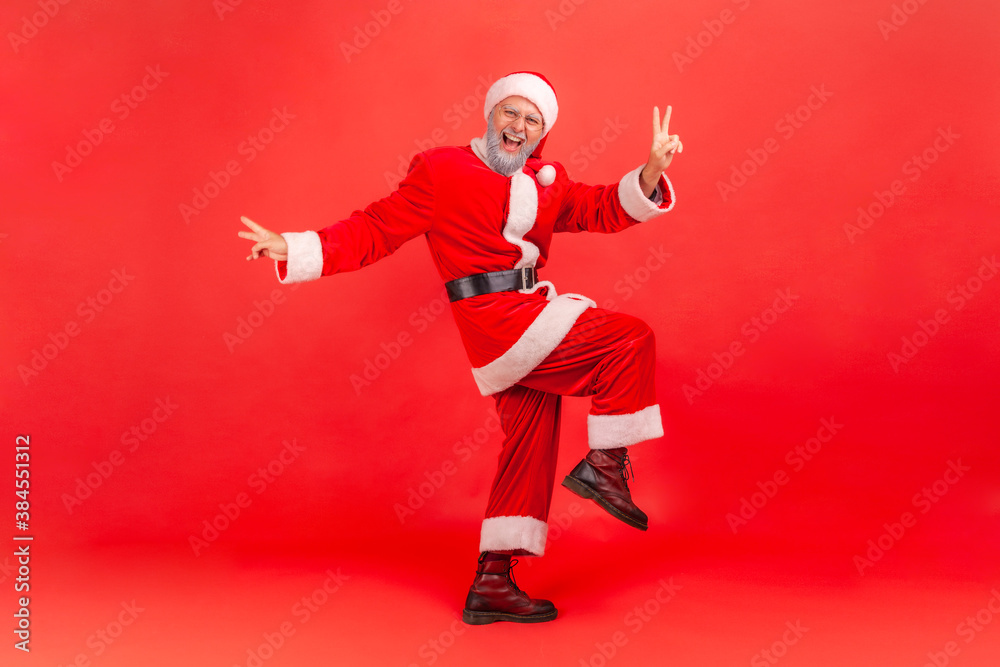 Full length portrait of happy positive man in santa claus costume jumping showing v gesture with fingers, celebrating victory, winter holidays coming. Indoor studio shot isolated on red background Full length portrait of happy positive man in santa claus costume jumping showing v gesture with fingers, celebrating victory, winter holidays coming. Indoor studio shot isolated on red background