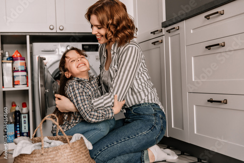 Child dabbles and embraces his beloved mother while sitting in kitchen near washing machine photo