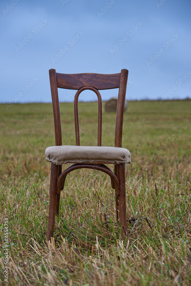 One old chair stands in a mown field against a cloudy sky. One old chair stands in a mown field against a cloudy sky.