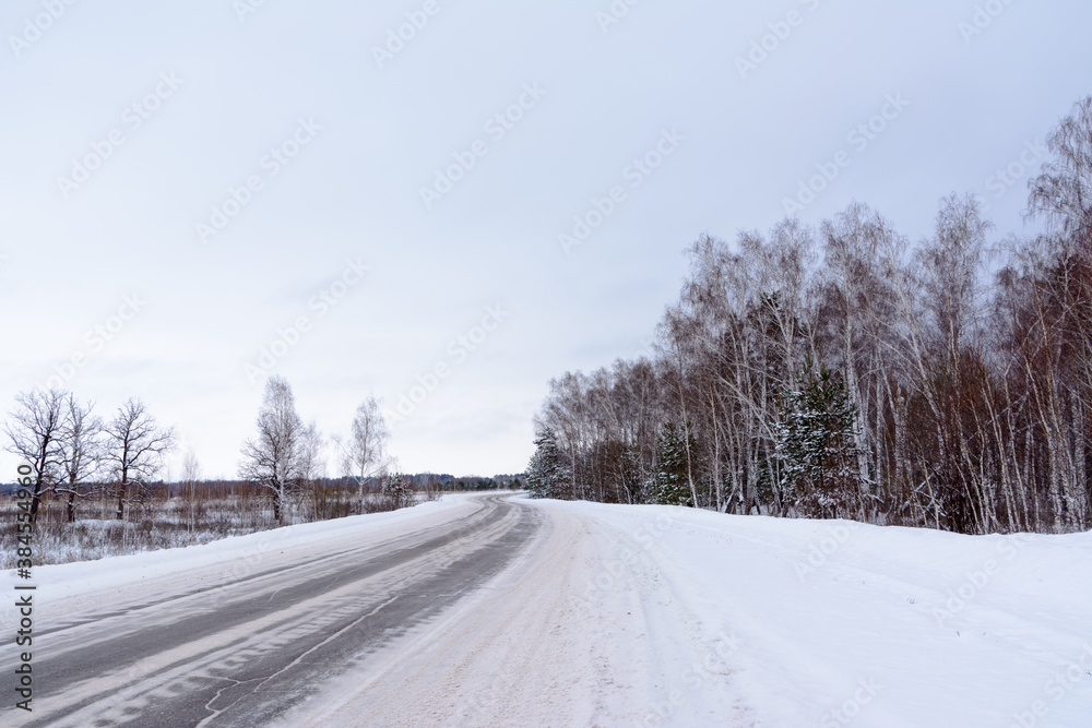 Patterns on the winter highway in the form of four straight lines. Snowy road on the background of snow-covered forest. Winter landscape.