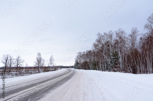 Patterns on the winter highway in the form of four straight lines. Snowy road on the background of snow-covered forest. Winter landscape. © Evgeniy