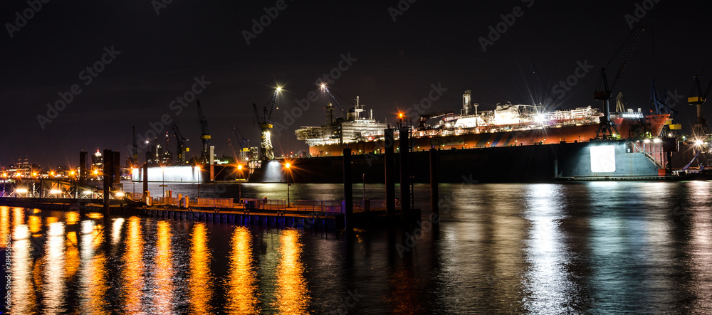 Scenic widescreen night shot of large container vessel under repair in the dock on the Elbe river in Hamburg, Germany