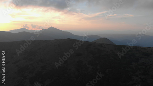 Dark mountain against the background of the rising sun. Gloomy foggy mountains and a cloudy sky illuminated by the first rays of the sun.