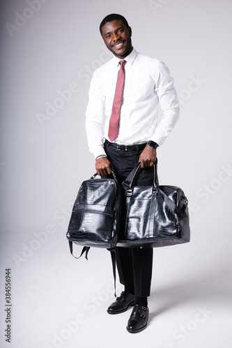 dark-skinned man holding a black backpack and a black leather bag. Stands on a white background