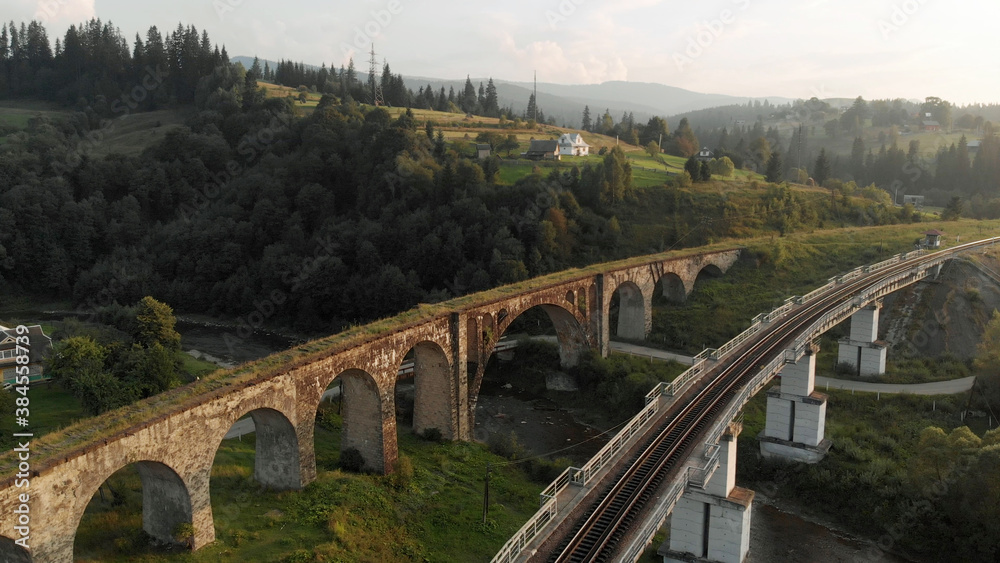 Industrial railroad over the river. Ancient bridge with beautiful arches. Gorgeous mountains on the horizon.