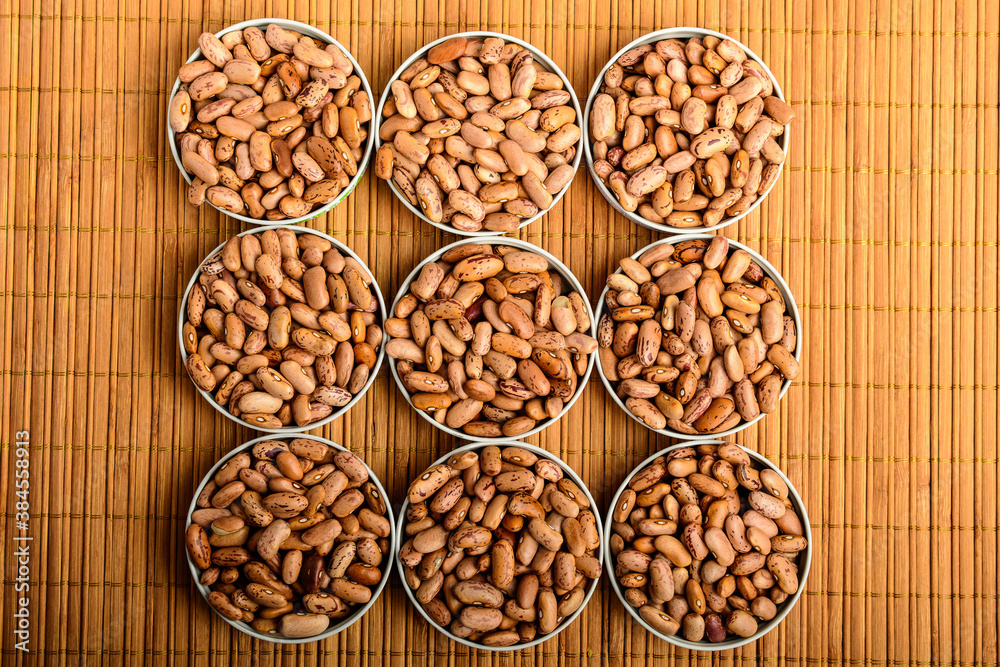 Top view of nine round bowls with many fresh organic red beans on a wooden table in warm light, brown monochrome indoor background photographed with selective focus. Top view of nine round bowls with many fresh organic red beans on a wooden table in warm light, brown monochrome indoor background photographed with selective focus.