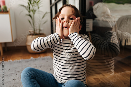 Little girl dabbles and blows her cheeks. Portrait of child sitting on floor