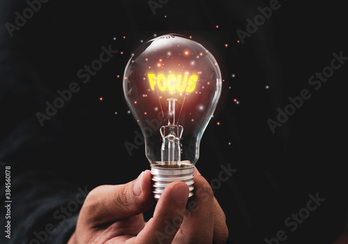 Focus objective target concept,Hand holding lightbulb which contain illuminating yellow focus wording.