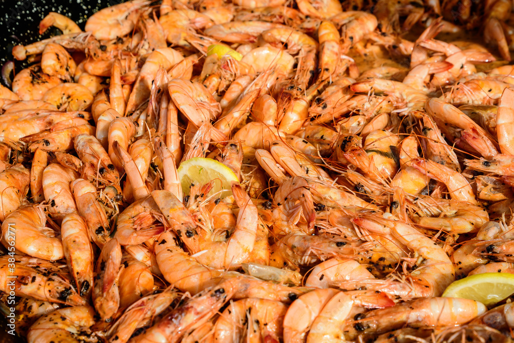 Close up of large portion of cooked shrimps with tomato sauce and yellow lemons in a large pan at a street food festival, ready to eat healthy seafood, beautiful orange monochrome outdoor background. Close up of large portion of cooked shrimps with tomato sauce and yellow lemons in a large pan at a street food festival, ready to eat healthy seafood, beautiful orange monochrome outdoor background.