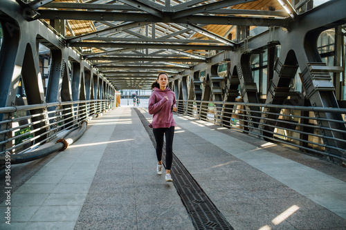Athletic young woman running on a steel girder walking bridge with a roof