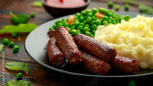 Vegetarian vegan sausages with mashed potato and green peas in black plate