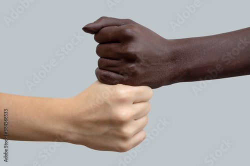 Black and white hands in the shape of fists, placed on top of each other. Grey isolated background. The concept of inter-racial friendship and respect, the fight against racism.