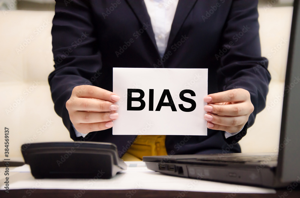 Obraz premium the word bias is written on a white piece of paper held by a business woman. personal opinions prejudice bias concept,