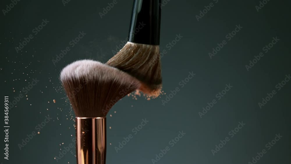 Makeup brushes touch each other on dark background and small particles of cosmetics, super slow motion, 1000 fps.