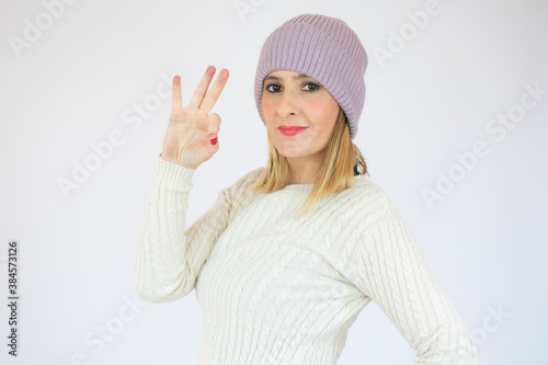 Beautiful young woman in winter clothes showing okay gesture on white background