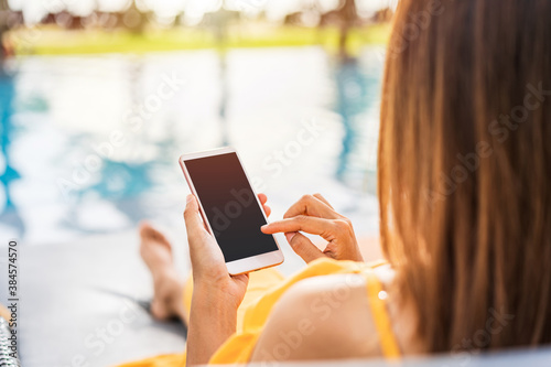 Young woman traveler relaxing and using a mobile phone by a hotel pool while traveling for summer vacation