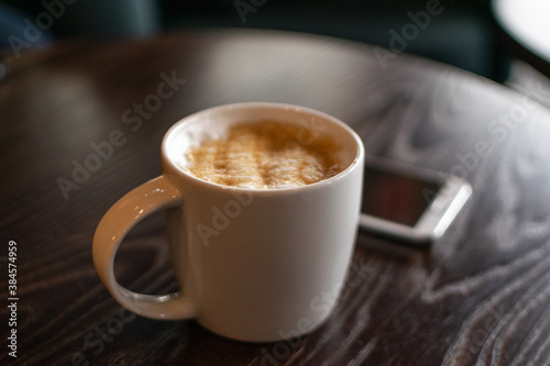 Coffee mug and mobile phone on the table closeup