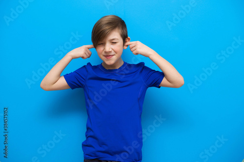 The child has covered his ears and is not listening. Close-up photo of a 9 year old boy. The boy does not listen to his parents and teachers. Photo of a naughty child on a blue background