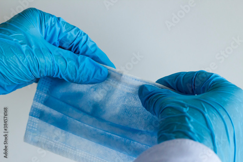 Hand in blue color rubber glove holding and checking wire of three ply surgical mask on gray background 