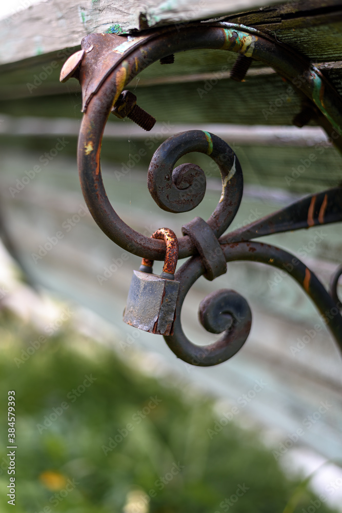 An old rusty lock hangs on the back of a rusty bench, close-up. Focus on the lock An old rusty lock hangs on the back of a rusty bench, close-up. Focus on the lock