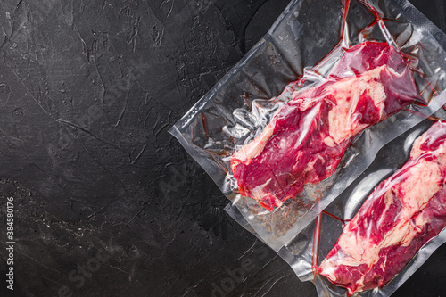 Chuck Tenders beef steak in vacuum sealed bag on black textured background top view space for text.