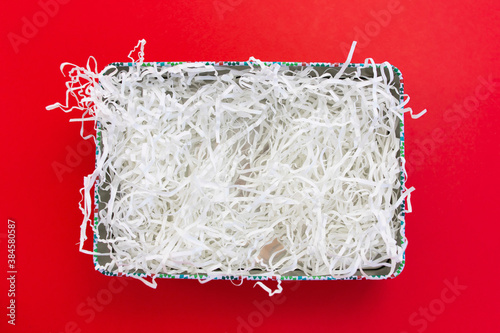White shredded paper packaging material in box flat lay on red background.