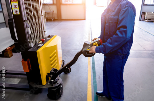 A worker in a warehouse uses a hand pallet stacker to transport pallets.