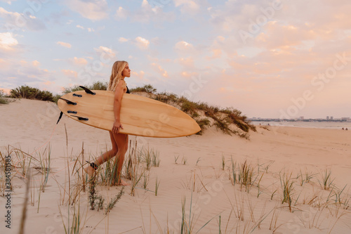 Surfer girl on sand beach with surfboard at warm sunset or sunrise. Attractive surfer on beach photo