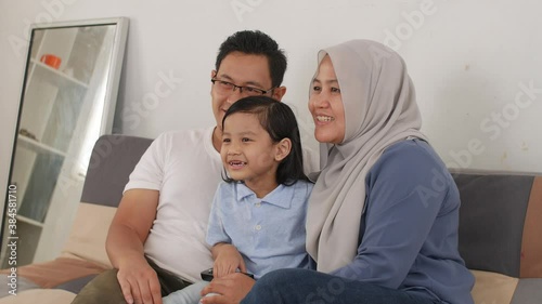 Happy muslim family watching tv. Asian father and mother spending quality time with their baby girl daughter watching movie at home 