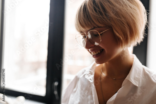 Amazing blonde girl laughing and looking down. Indoor shot of charming young woman in glasses.