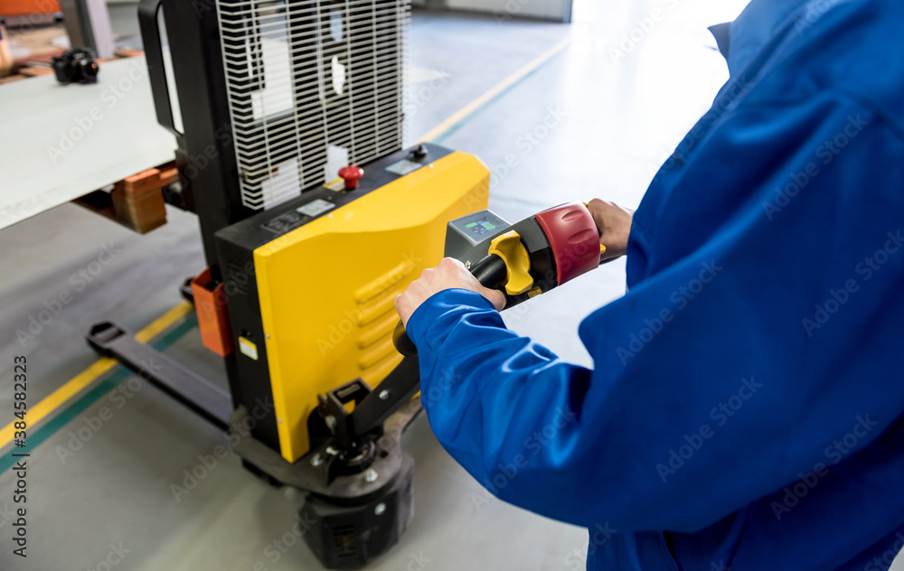 A worker in a warehouse uses a hand pallet stacker to transport pallets. A worker in a warehouse uses a hand pallet stacker to transport pallets.