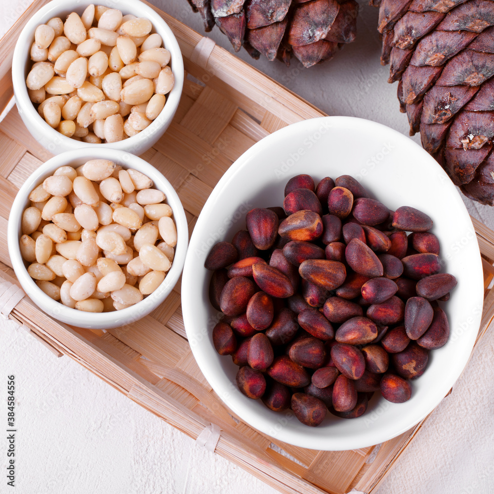 Shelled and unshelled pine nuts and pine cones on the white table Shelled and unshelled pine nuts and pine cones on the white table