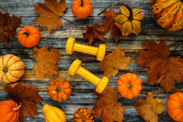 Two yellow dumbbells with various pumpkins, squashes and autumn leaves. Healthy fitness lifestyle fall composition, flat lay.