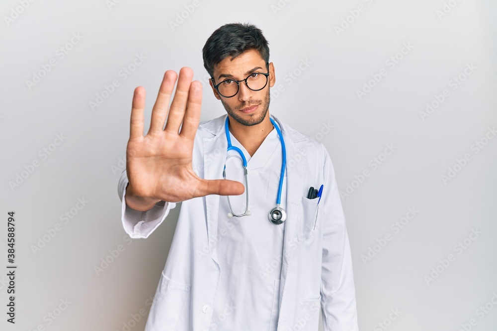 Young handsome man wearing doctor uniform and stethoscope doing stop sing with palm of the hand. warning expression with negative and serious gesture on the face. Young handsome man wearing doctor uniform and stethoscope doing stop sing with palm of the hand. warning expression with negative and serious gesture on the face.