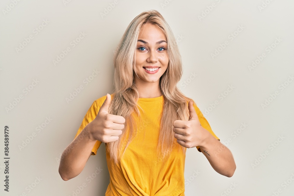 Obraz premium Beautiful caucasian blonde girl wearing casual tshirt success sign doing positive gesture with hand, thumbs up smiling and happy. cheerful expression and winner gesture.
