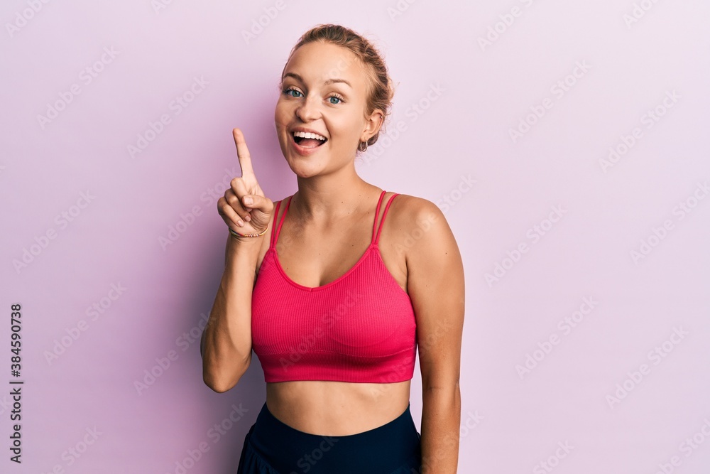 Beautiful caucasian woman wearing sportswear showing and pointing up with finger number one while smiling confident and happy.