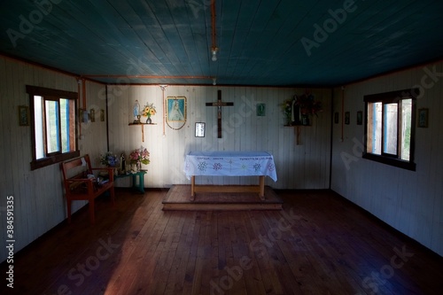 intérieur d'une petite chapelle vide en bois au Chili très simple et rudimentaire avec un rayon de lumière illuminant le mur du fond
