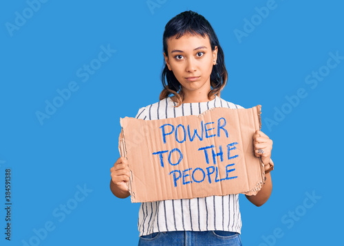 Young woman holding power to the people banner thinking attitude and sober expression looking self confident