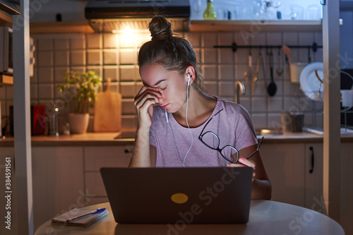  Tired stressed woman workaholic in headphones holding eyeglasses and massaging his nose bridge while watching webinar online on laptop late in the evening photo