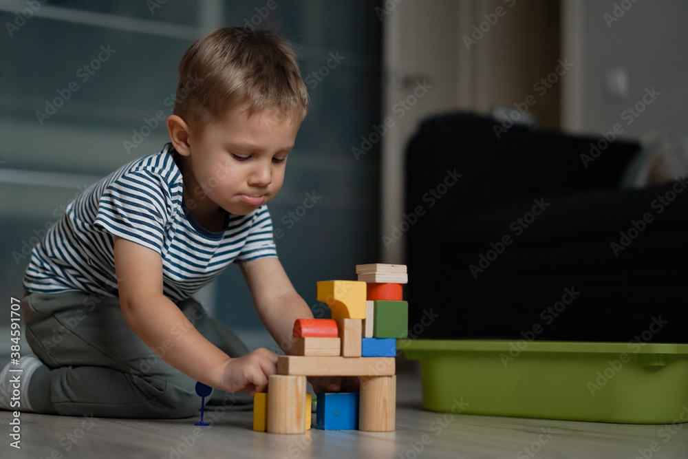 Adorable little caucasian boy making funny face and playing with a tower out of colorful wooden blocks Adorable little caucasian boy making funny face and playing with a tower out of colorful wooden blocks