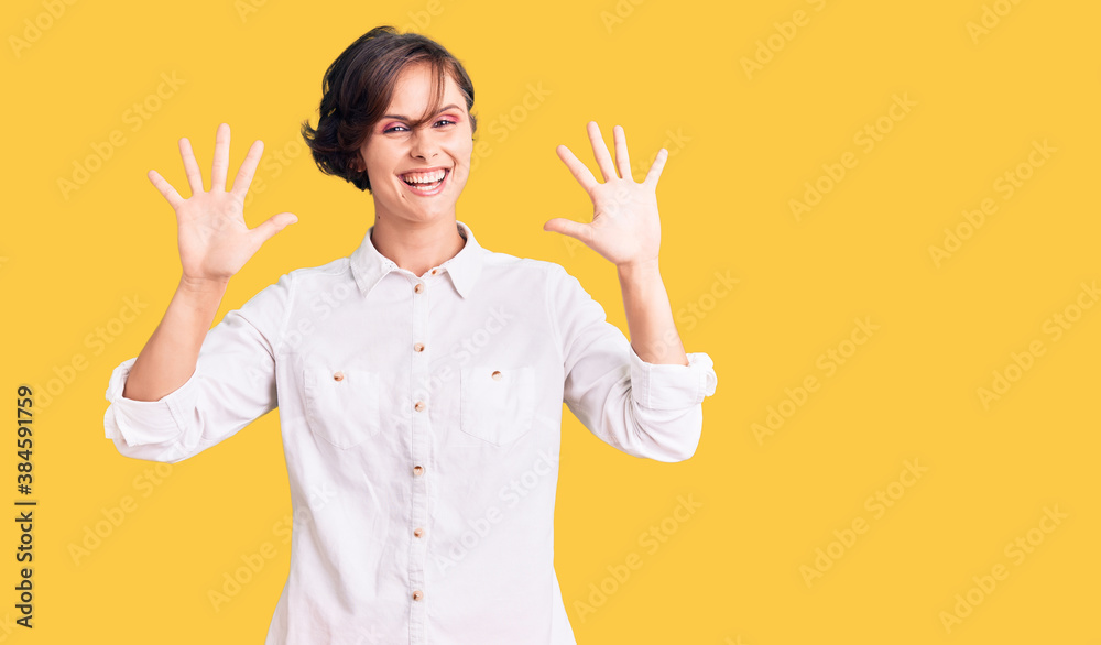 Beautiful young woman with short hair wearing elegant white shirt showing and pointing up with fingers number ten while smiling confident and happy.