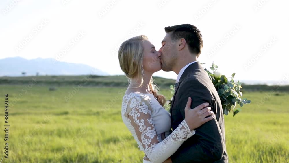 Happy Newlywed Couple Hugging And Kissing On Nature Landscape Under Clear Sky. - Medium Shot Happy Newlywed Couple Hugging And Kissing On Nature Landscape Under Clear Sky. - Medium Shot