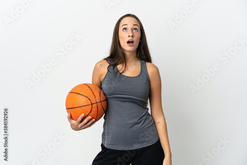 Young woman playing basketball over isolated white background looking up and with surprised expression