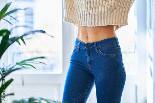 Beautiful slim waist with navel. Skinny figure of a woman in a white warm sweater and jeans. Healthy female body photo