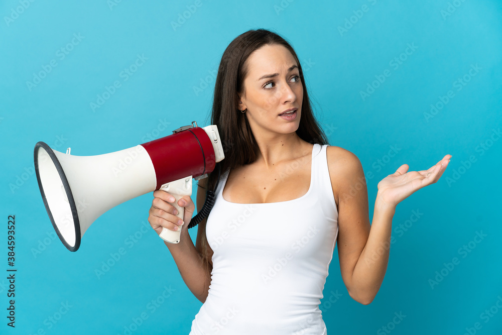 Young hispanic woman over isolated blue background holding a megaphone and with surprise facial expression Young hispanic woman over isolated blue background holding a megaphone and with surprise facial expression