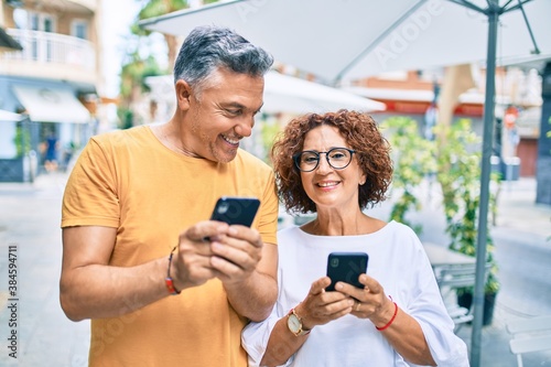 Middle age couple smiling happy using smartphone at street of city.