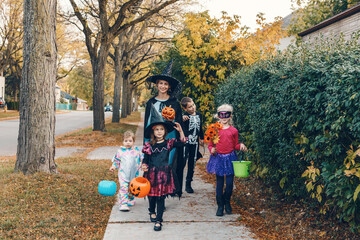 Trick or treat. Mother with children going to trick or treat on Halloween holiday. Mom with kids in party costumes with baskets going to neighbourhood homes for candies, treats.