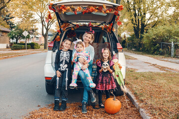 Trick or trunk. Family celebrating Halloween in trunk of car. Mother with three children kids celebrating traditional October holiday outdoors. Social distance and safe alternative celebration.
